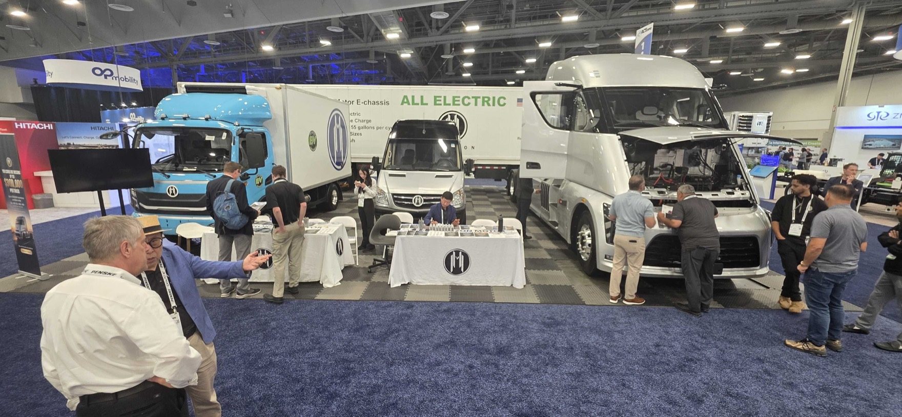 iMatrix at Horizon Motors Booth 1443, ACT Expo 2026 — three Horizon Motors all-electric trucks on display: a blue Class 8 cabover, a white E-chassis delivery van, and a white Class 8 sleeper tractor with hood open